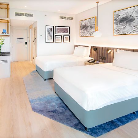 Radisson Blu Hotel & Resort, Abu Dhabi Corniche Extérieur photo The image shows a modern hotel room featuring two double beds with white linens. The room has a light and airy ambiance, with wooden flooring and a complementary area rug. There are decorative wall frames with artwork above the beds, and a stylish pe