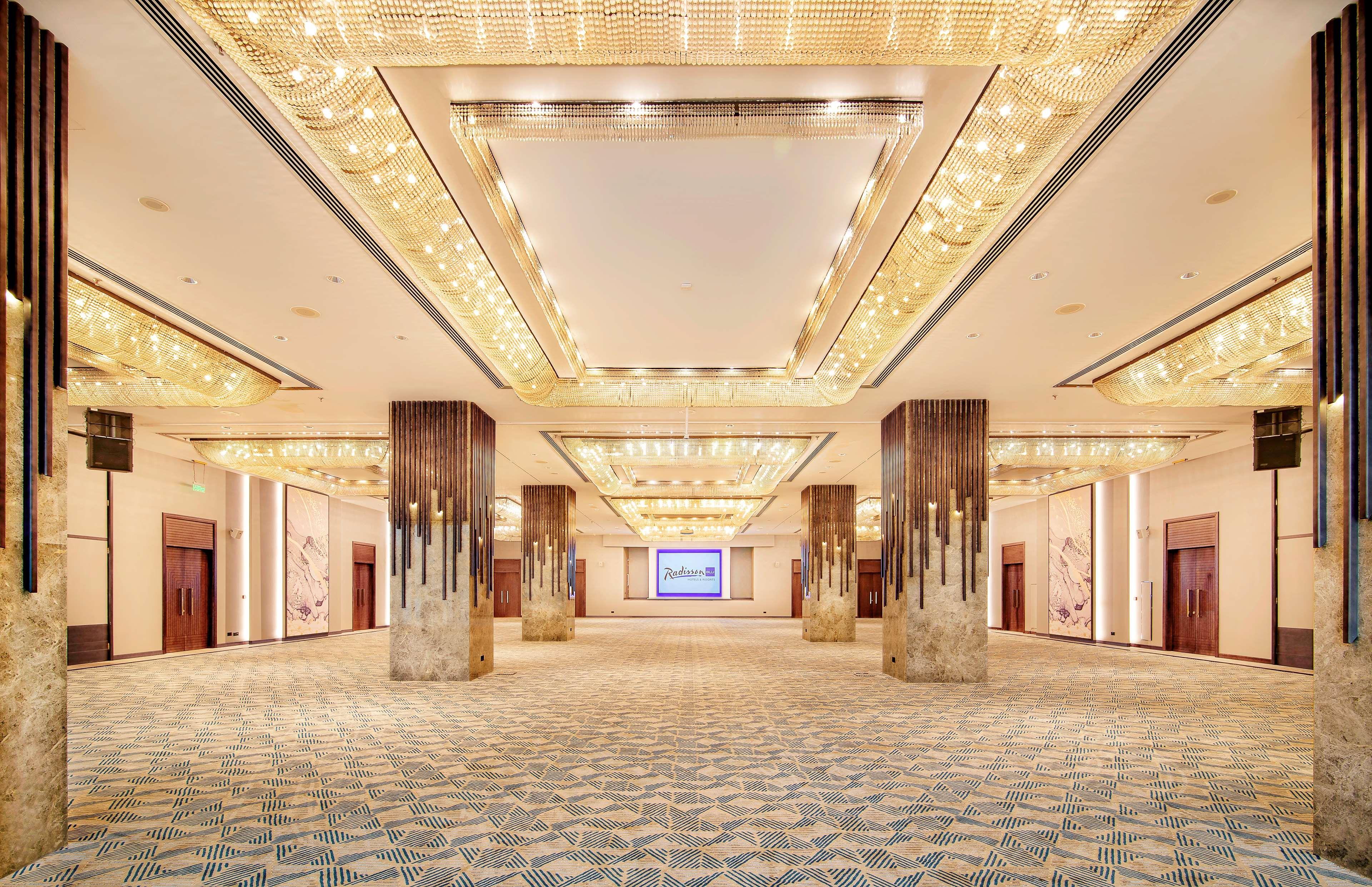 Radisson Blu Hotel & Resort, Abu Dhabi Corniche Extérieur photo The photo depicts a spacious and elegantly designed interior hall, likely part of a conference or event venue. The ceiling features decorative lighting elements, providing a warm and luxurious ambiance. There are large pillars that frame the space, a