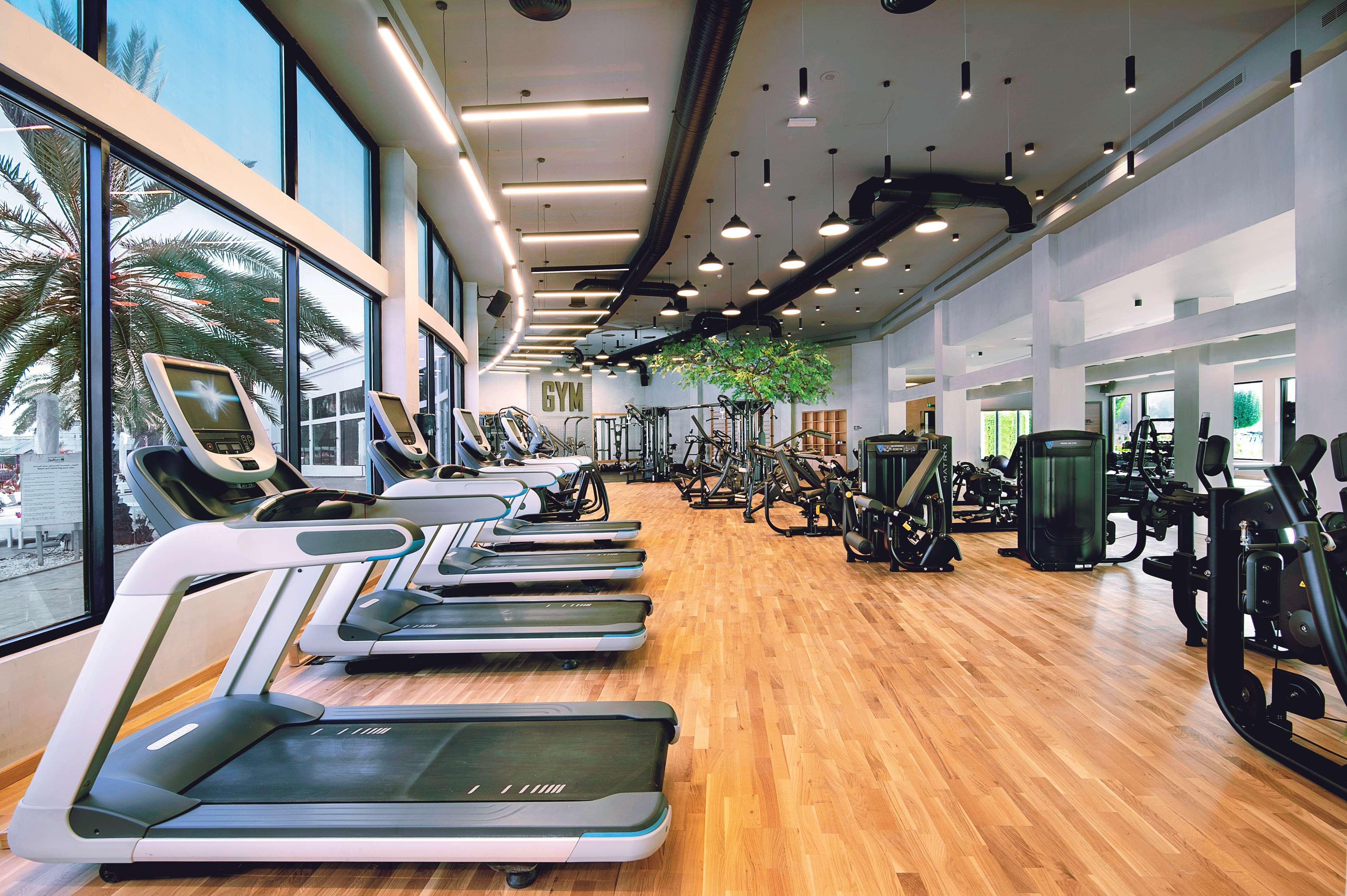 Radisson Blu Hotel & Resort, Abu Dhabi Corniche Extérieur photo The photo shows a modern gym interior with numerous exercise machines. In the foreground, there are several treadmills positioned side by side on a wooden floor. The gym features large windows that let in natural light and provide a view of greenery 