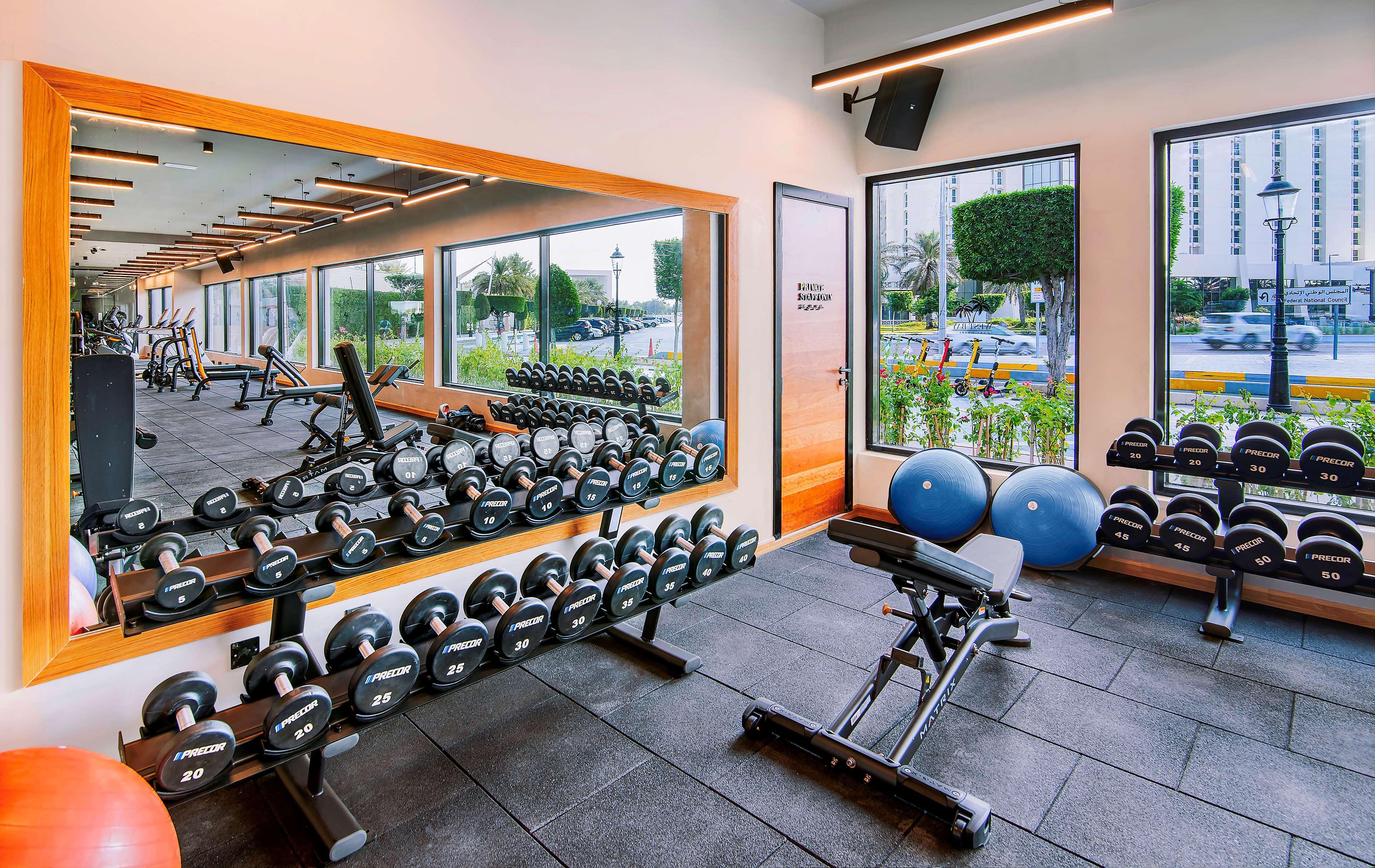 Radisson Blu Hotel & Resort, Abu Dhabi Corniche Extérieur photo The photo shows a modern gym interior featuring various workout equipment. On one side, there is a row of dumbbells neatly arranged on a rack. In the center, a workout bench is positioned, likely for strength training exercises. There are also exerci