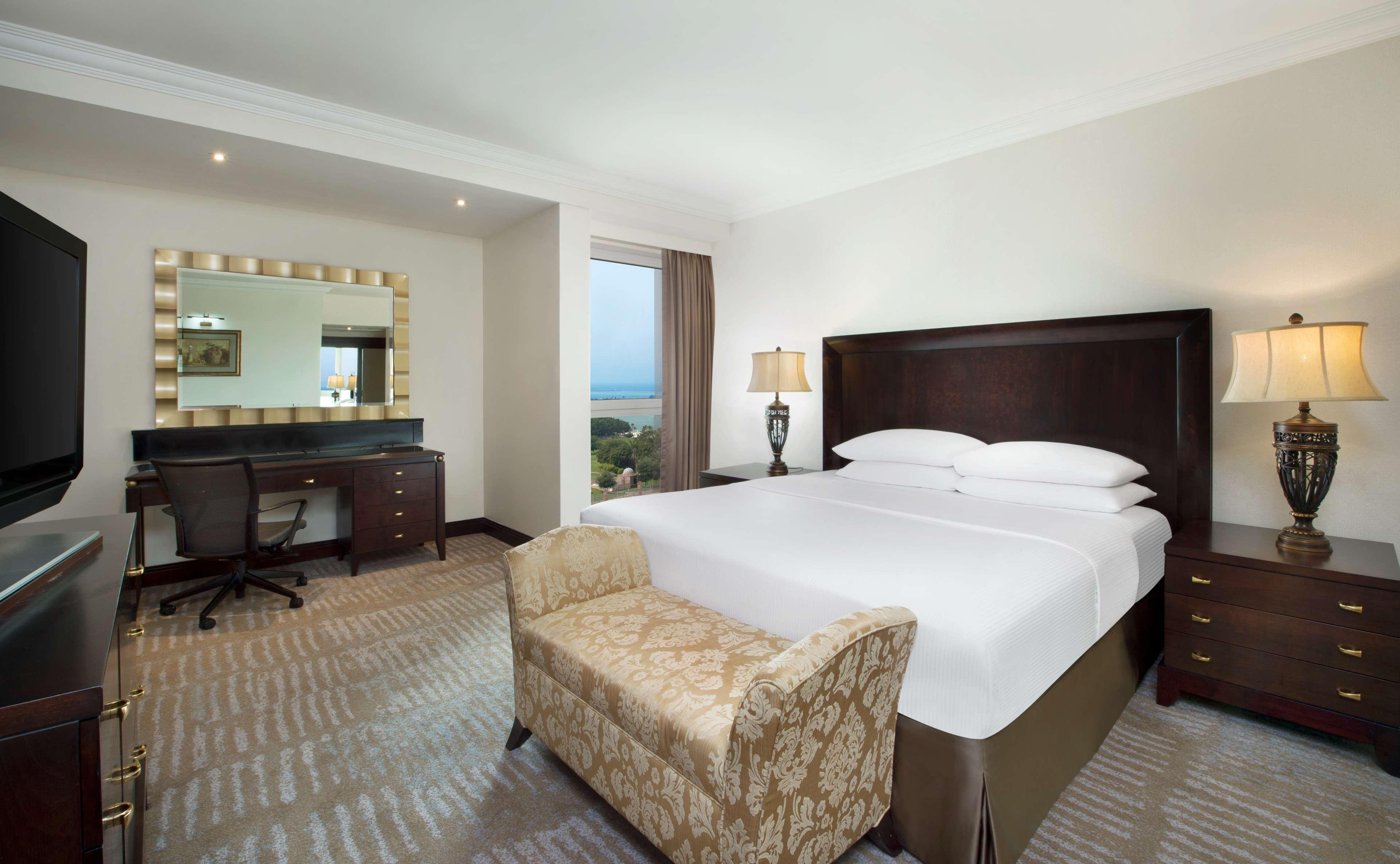 Radisson Blu Hotel & Resort, Abu Dhabi Corniche Extérieur photo The photo shows a well-decorated hotel room featuring a comfortable king-sized bed with crisp white linens. There’s a stylish armchair at the foot of the bed. To one side, there's a desk with a chair, providing a workspace. A large mirror with a deco