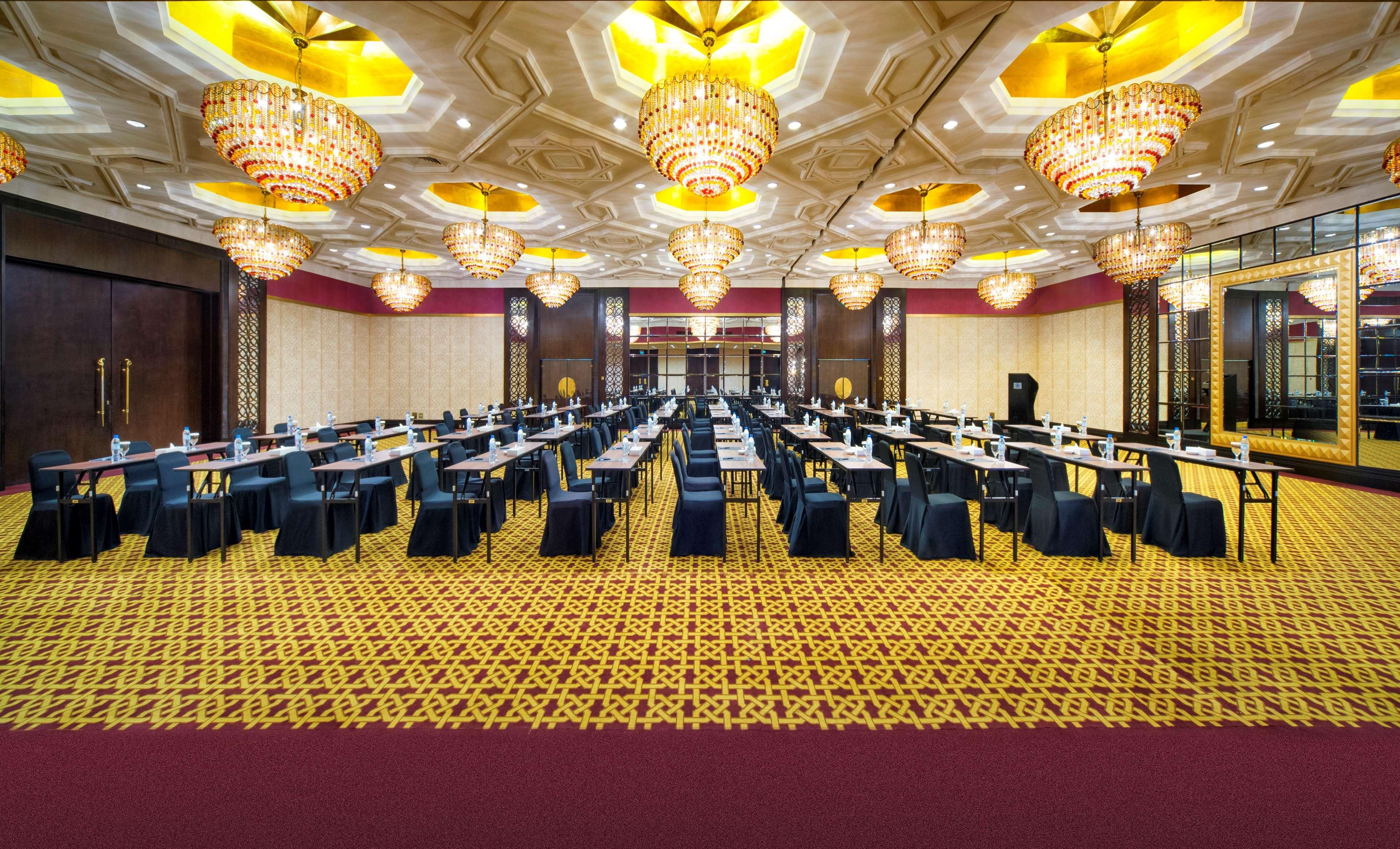Radisson Blu Hotel & Resort, Abu Dhabi Corniche Extérieur photo The image displays a banquet or conference hall with a luxurious interior. The room features a lavish ceiling adorned with intricate designs and multiple large chandeliers that provide bright lighting. There are long tables arranged in rows, each cov