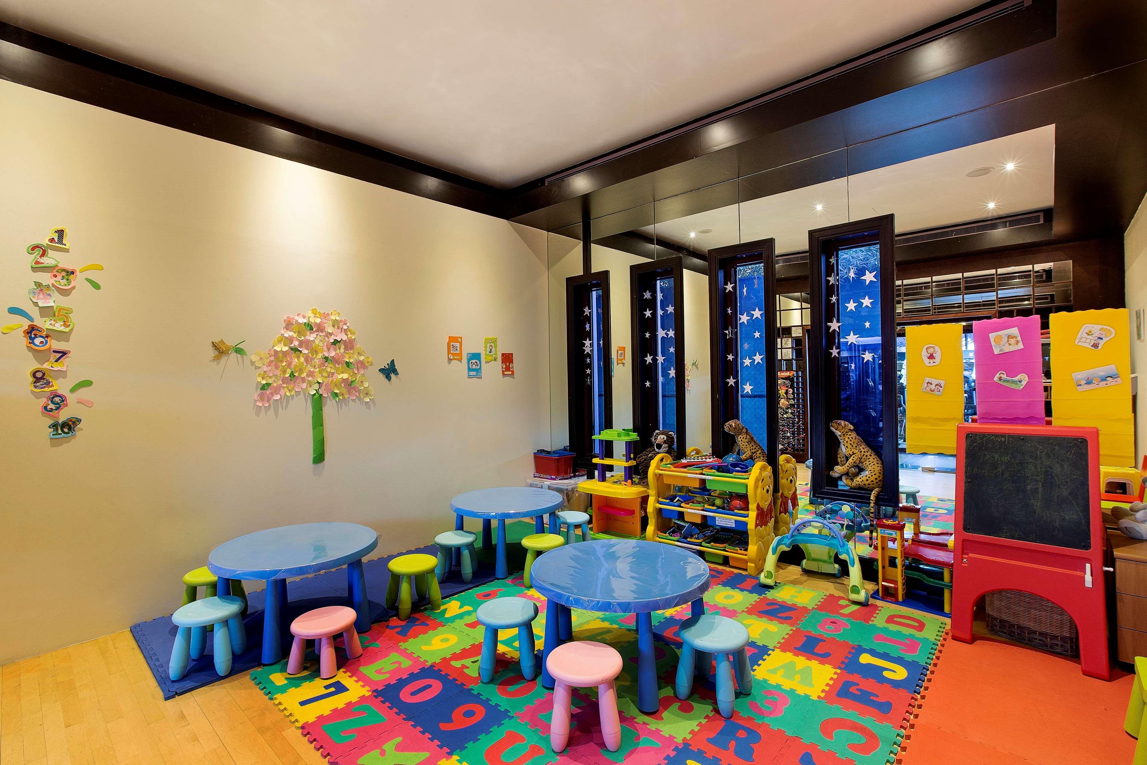 Radisson Blu Hotel & Resort, Abu Dhabi Corniche Extérieur photo The photo shows a colorful and playful interior, likely a children's playroom or classroom. There are small blue tables surrounded by brightly colored stools in various pastel shades. The floor is covered with a multi-colored mat featuring letters an