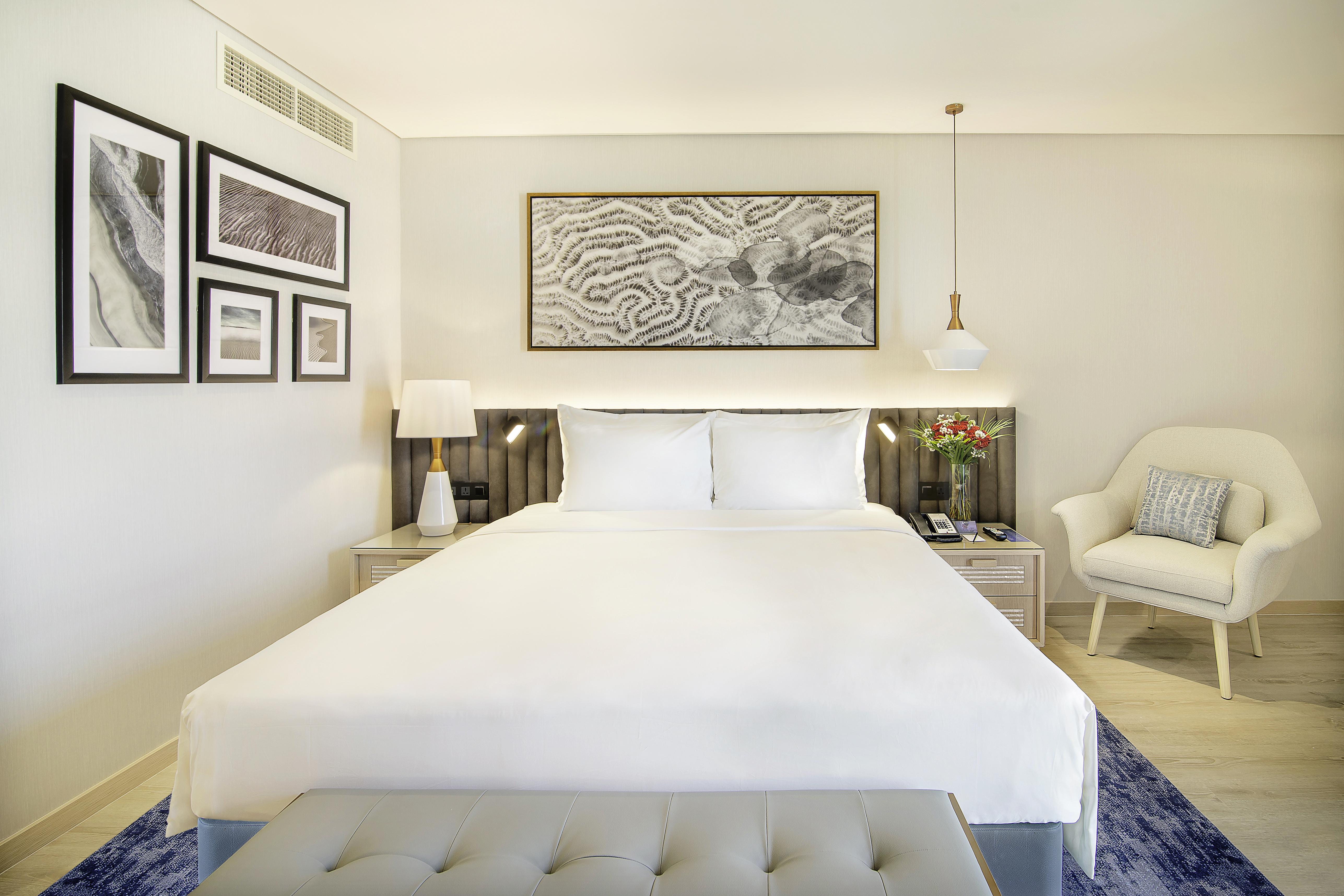 Radisson Blu Hotel & Resort, Abu Dhabi Corniche Extérieur photo The photo shows a well-decorated hotel room featuring a king-sized bed with crisp white linens. There are two bedside tables, each with a lamp, on either side of the bed. Above the bed is a large framed artwork, adding a touch of elegance to the spac
