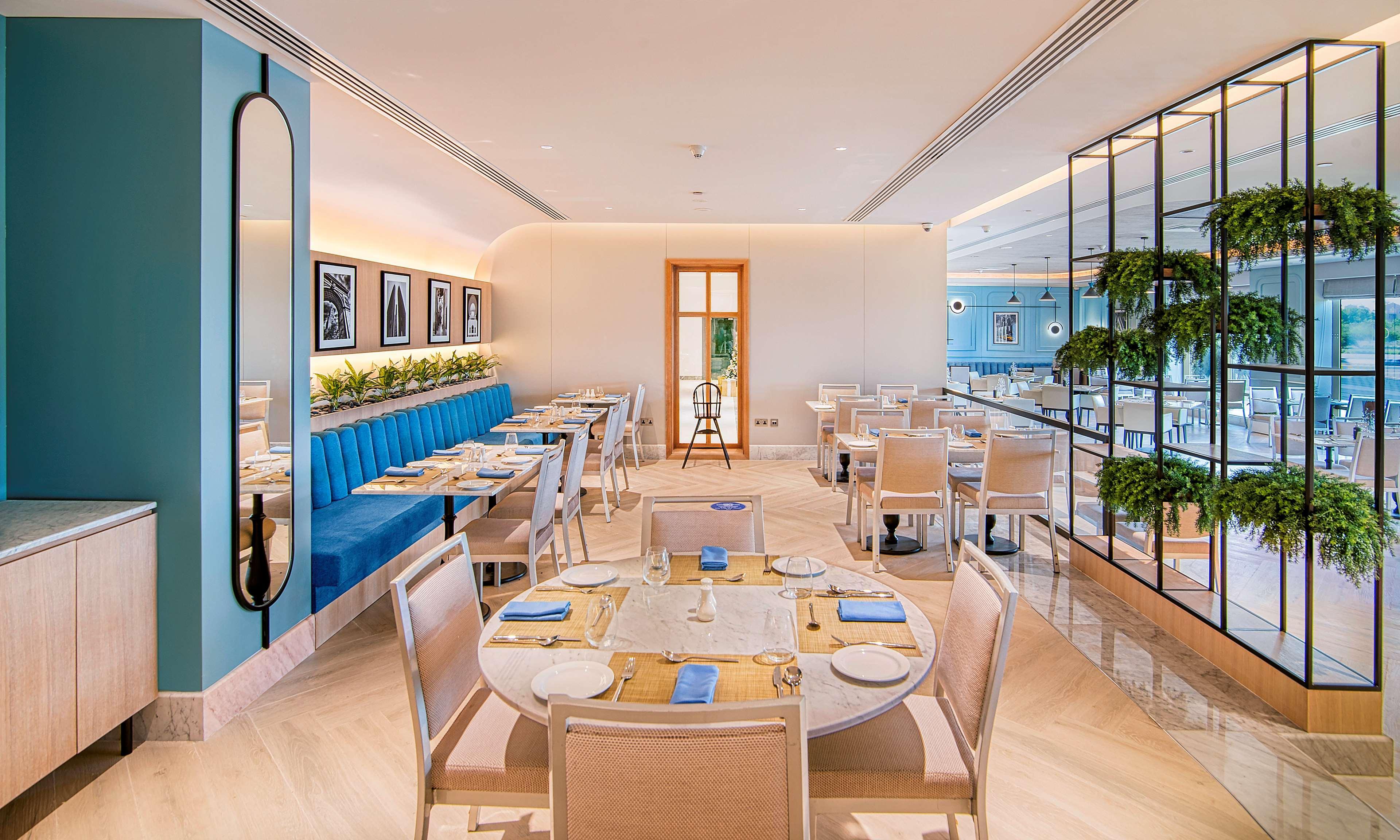 Radisson Blu Hotel & Resort, Abu Dhabi Corniche Extérieur photo The photo showcases a modern restaurant interior. It features a mix of light and vibrant colors, with blue upholstered seating along one wall. Tables are elegantly set with blue napkins and white dishware. The space has a bright, airy feel, enhanced 