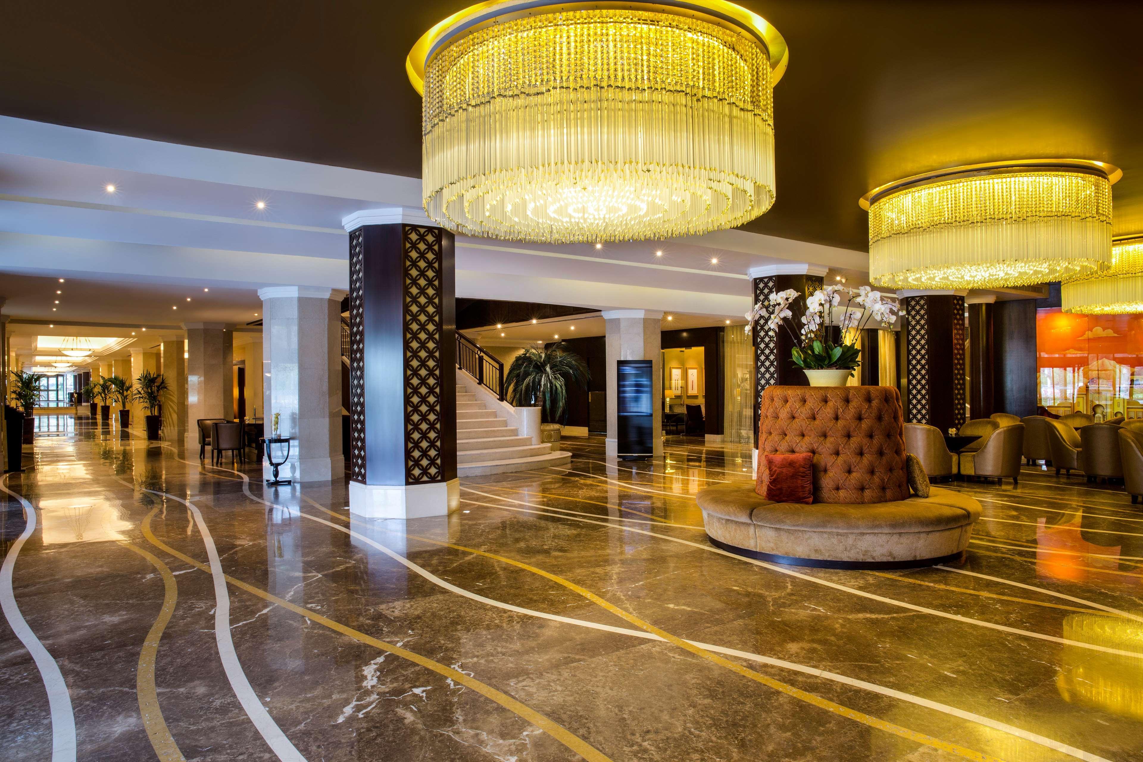 Radisson Blu Hotel & Resort, Abu Dhabi Corniche Extérieur photo The photo depicts an elegant hotel lobby with a luxurious ambiance. The flooring is made of polished marble, featuring decorative swirling lines. There are two large, ornate chandeliers hanging from the ceiling, providing warm lighting. Column suppor
