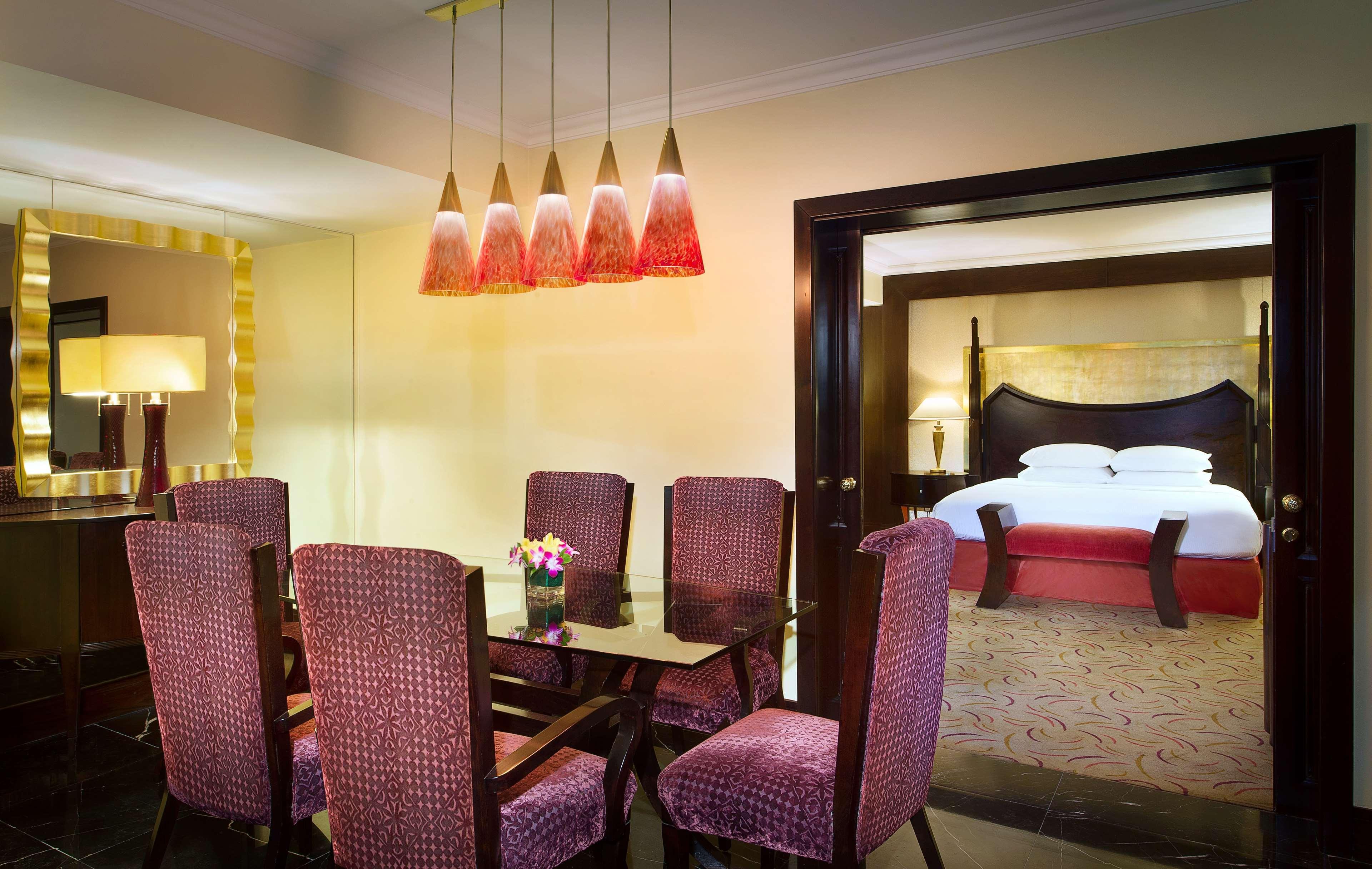 Radisson Blu Hotel & Resort, Abu Dhabi Corniche Extérieur photo The photo shows an elegantly decorated room featuring a dining area and a connected bedroom. The dining space has a glass table surrounded by upholstered chairs in a rich, deep color. Above the table, there are multiple pendant lights with a modern d