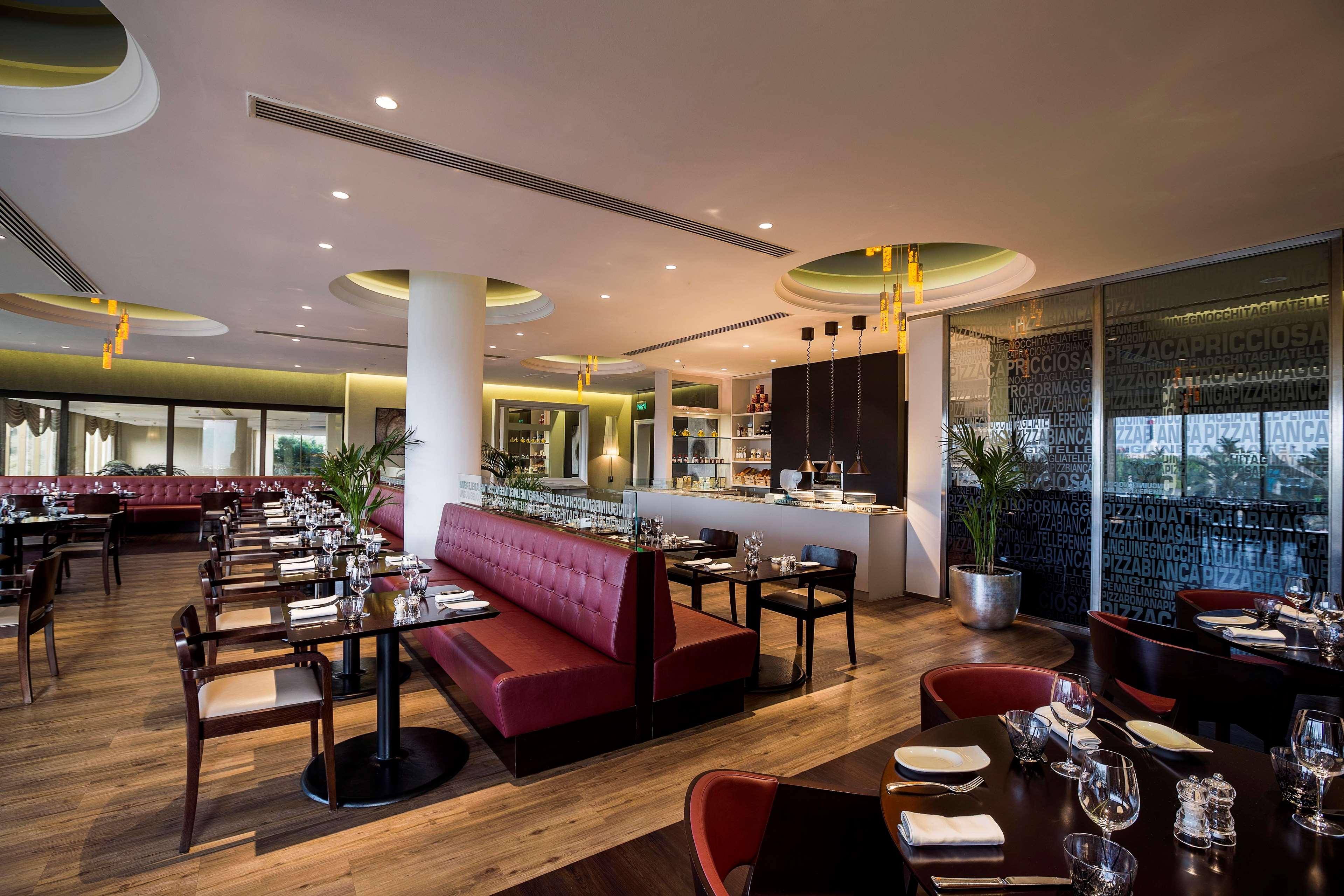 Radisson Blu Hotel & Resort, Abu Dhabi Corniche Extérieur photo The photo shows a modern restaurant interior with a stylish design. It features a mix of dark wood and plush upholstery, with booths and tables arranged neatly. The booths are upholstered in a deep red fabric, while the tables are set with cutlery an