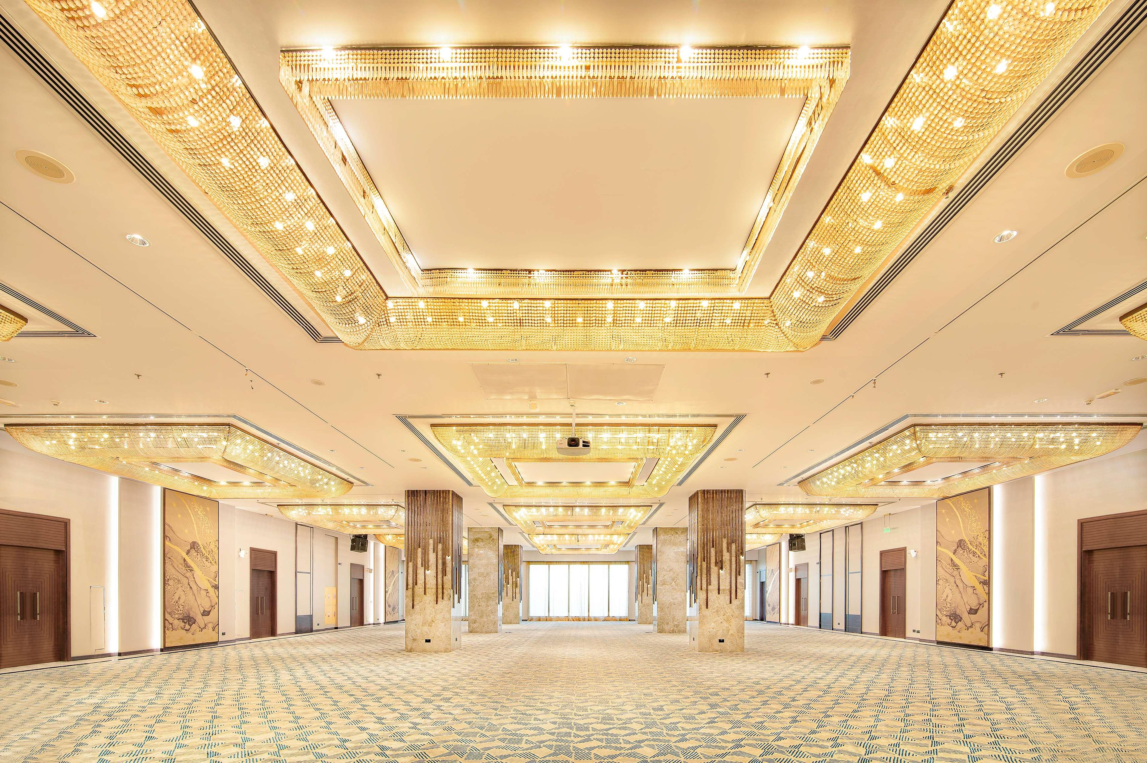 Radisson Blu Hotel & Resort, Abu Dhabi Corniche Extérieur photo The photo shows a spacious, elegantly designed interior, likely a banquet or conference hall. The ceiling features a luxurious design with intricate lighting elements that give off a warm glow. The floor is covered with a patterned carpet in soft col