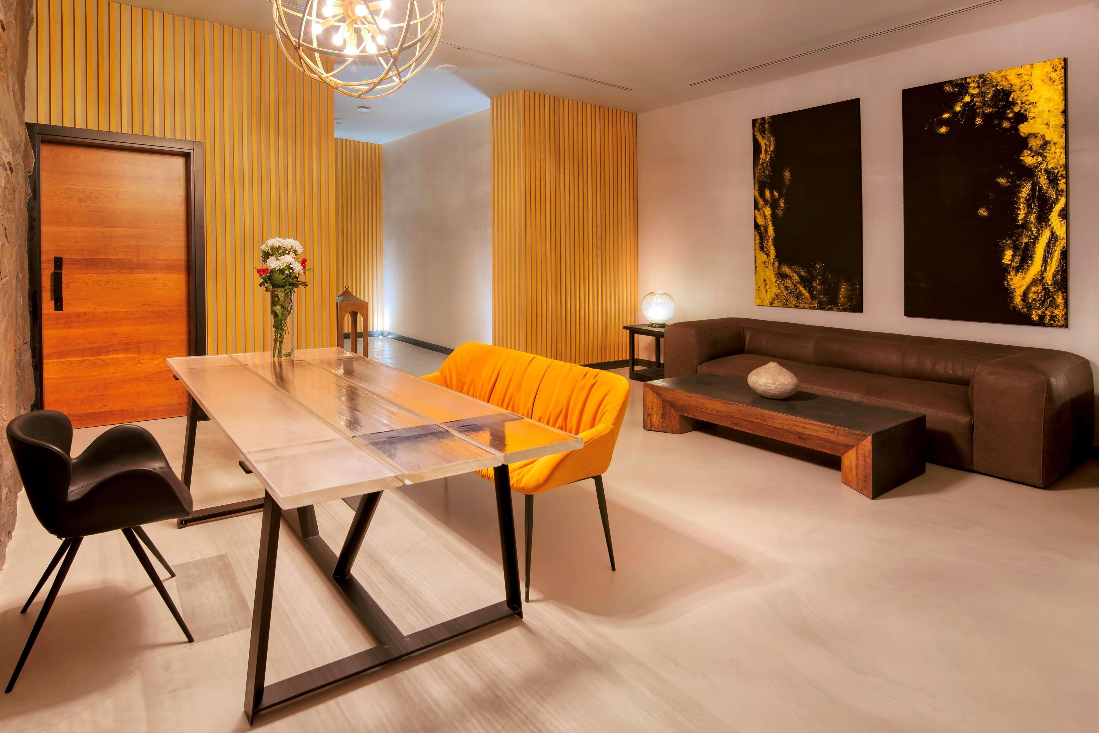 Radisson Blu Hotel & Resort, Abu Dhabi Corniche Extérieur photo The photo shows a modern and stylish interior space. There is a minimalist dining or meeting table made of glass and metal, surrounded by black chairs. One of the chairs is bright orange, adding a pop of color to the room. In the background, there is