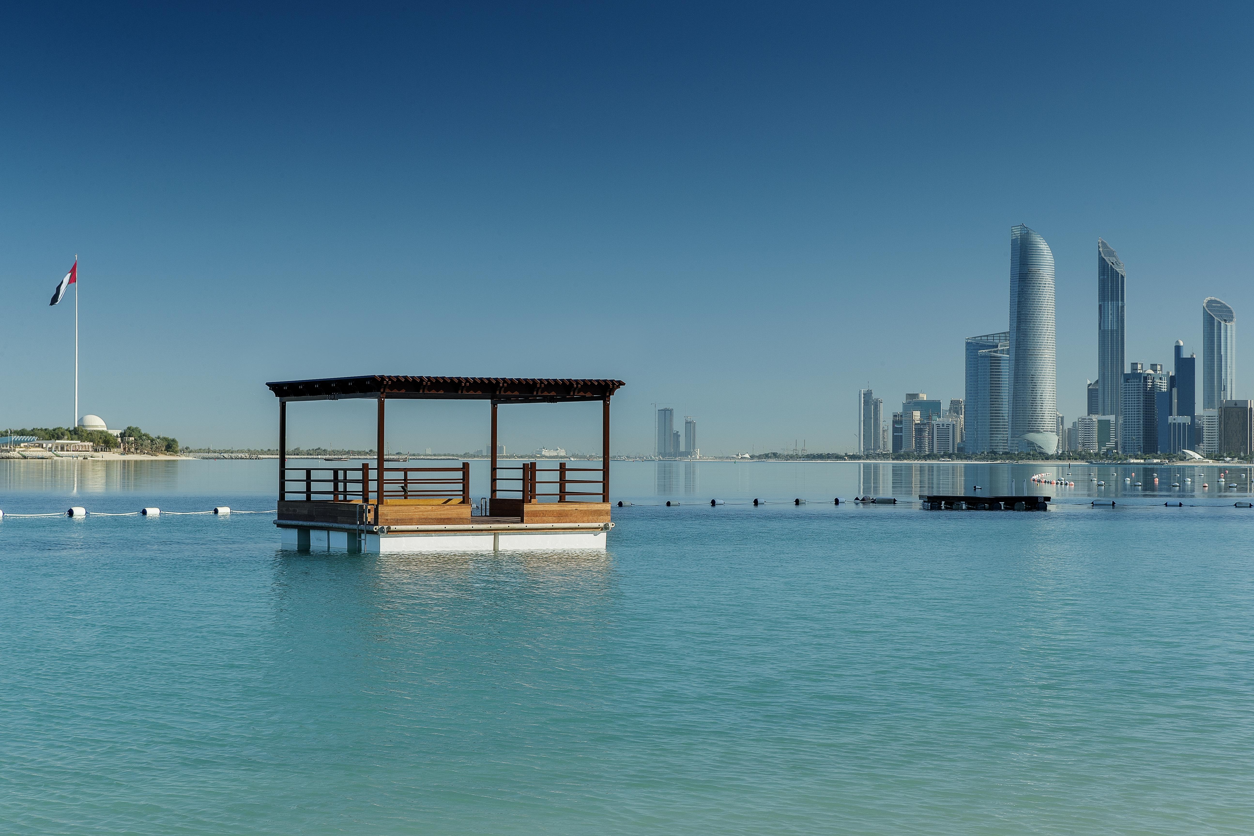 Radisson Blu Hotel & Resort, Abu Dhabi Corniche Extérieur photo The photo depicts a serene body of water with a small wooden structure or gazebo situated on it. The structure has a roof and seating area, creating a peaceful spot for relaxation. In the background, there are tall modern buildings, suggesting an urb
