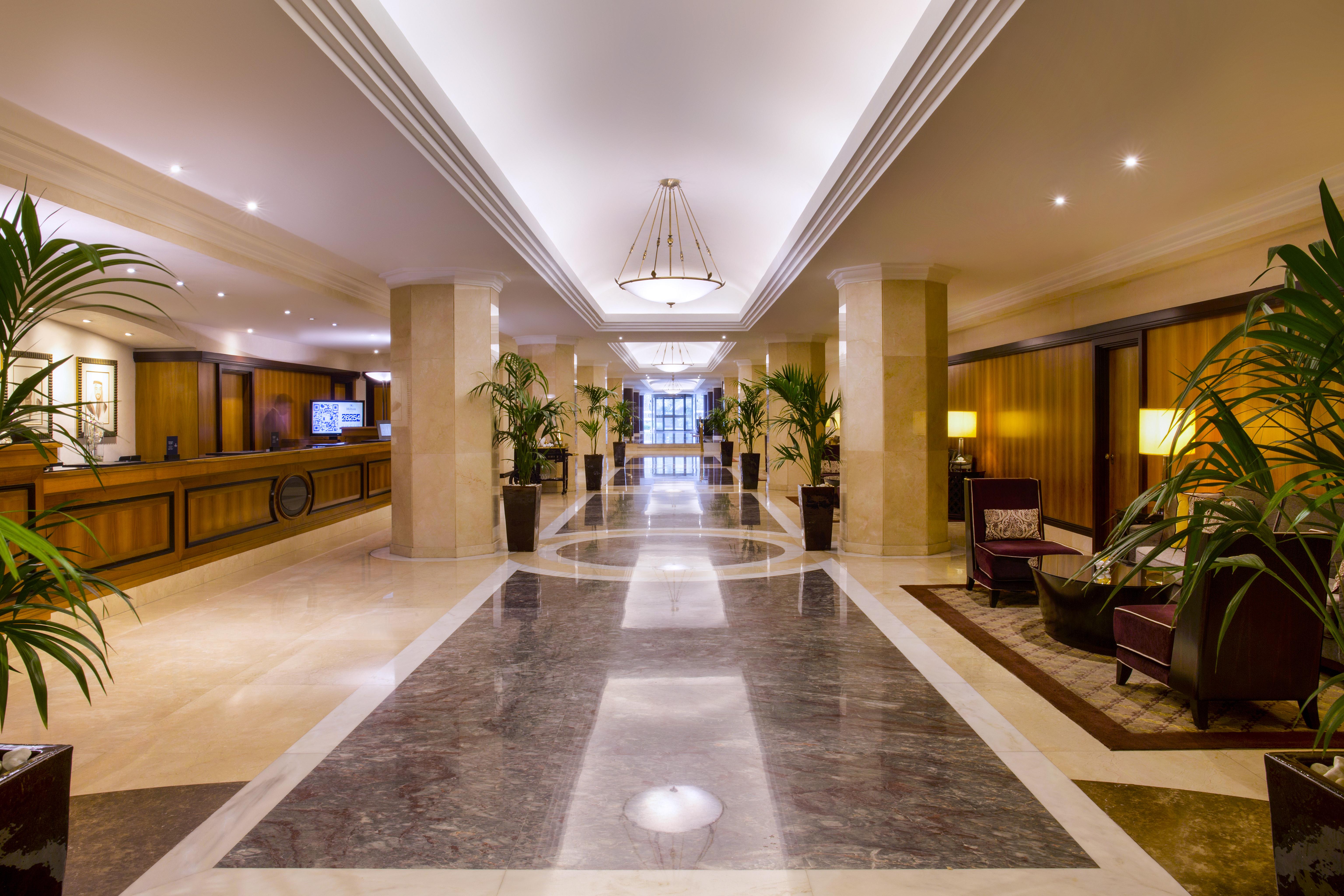 Radisson Blu Hotel & Resort, Abu Dhabi Corniche Extérieur photo The photo displays an elegant hotel lobby. It features a spacious hallway with polished marble flooring and decorative lighting. On either side of the corridor are tall potted plants, adding a touch of greenery to the space. The reception desk is vis