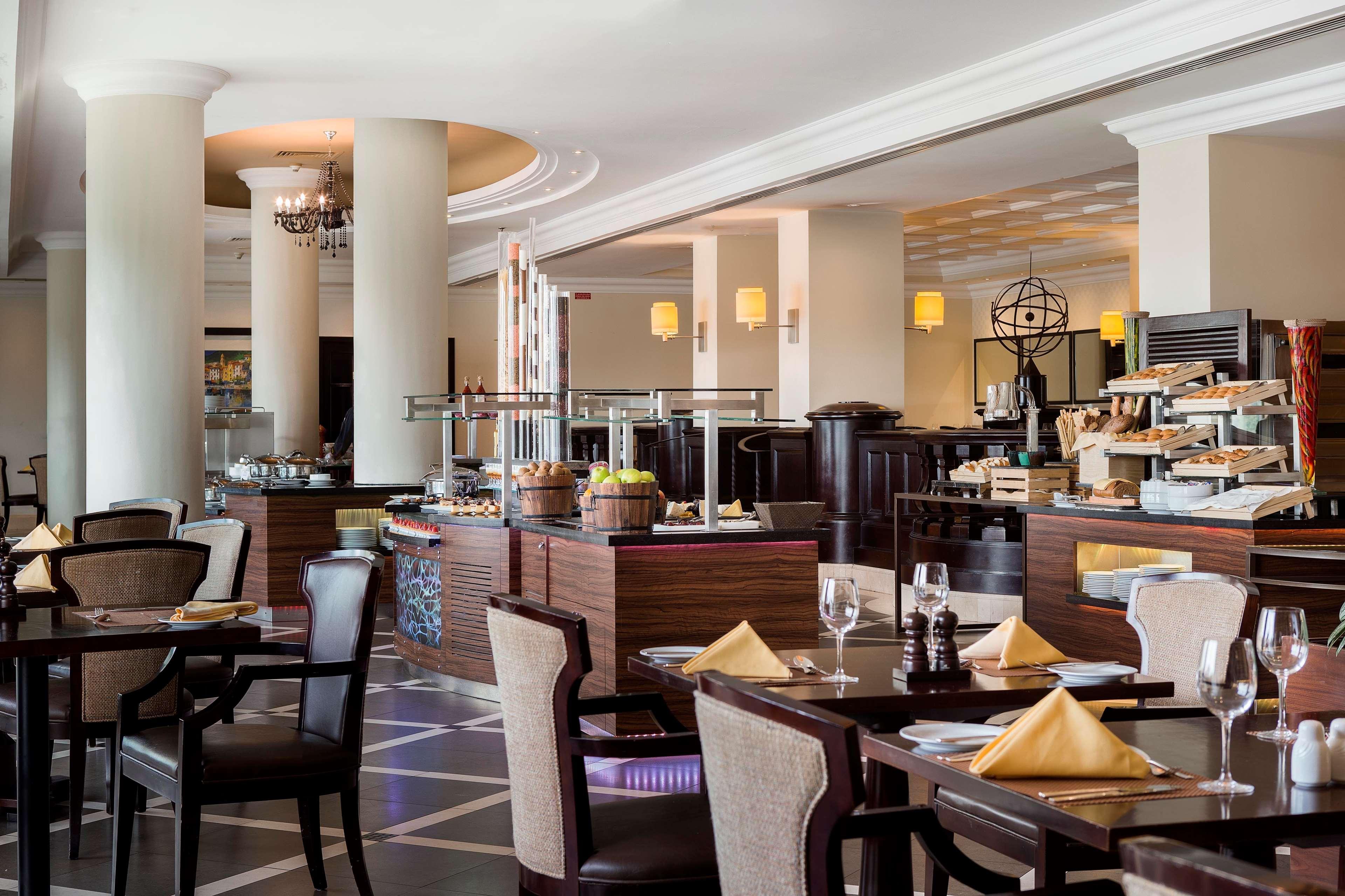 Radisson Blu Hotel & Resort, Abu Dhabi Corniche Extérieur photo The photo shows an elegant dining area of a restaurant. There are well-set tables with dark wooden furniture, featuring white tablecloths and neatly folded yellow napkins. The restaurant has a modern decor, with large pillars and ambient lighting fro