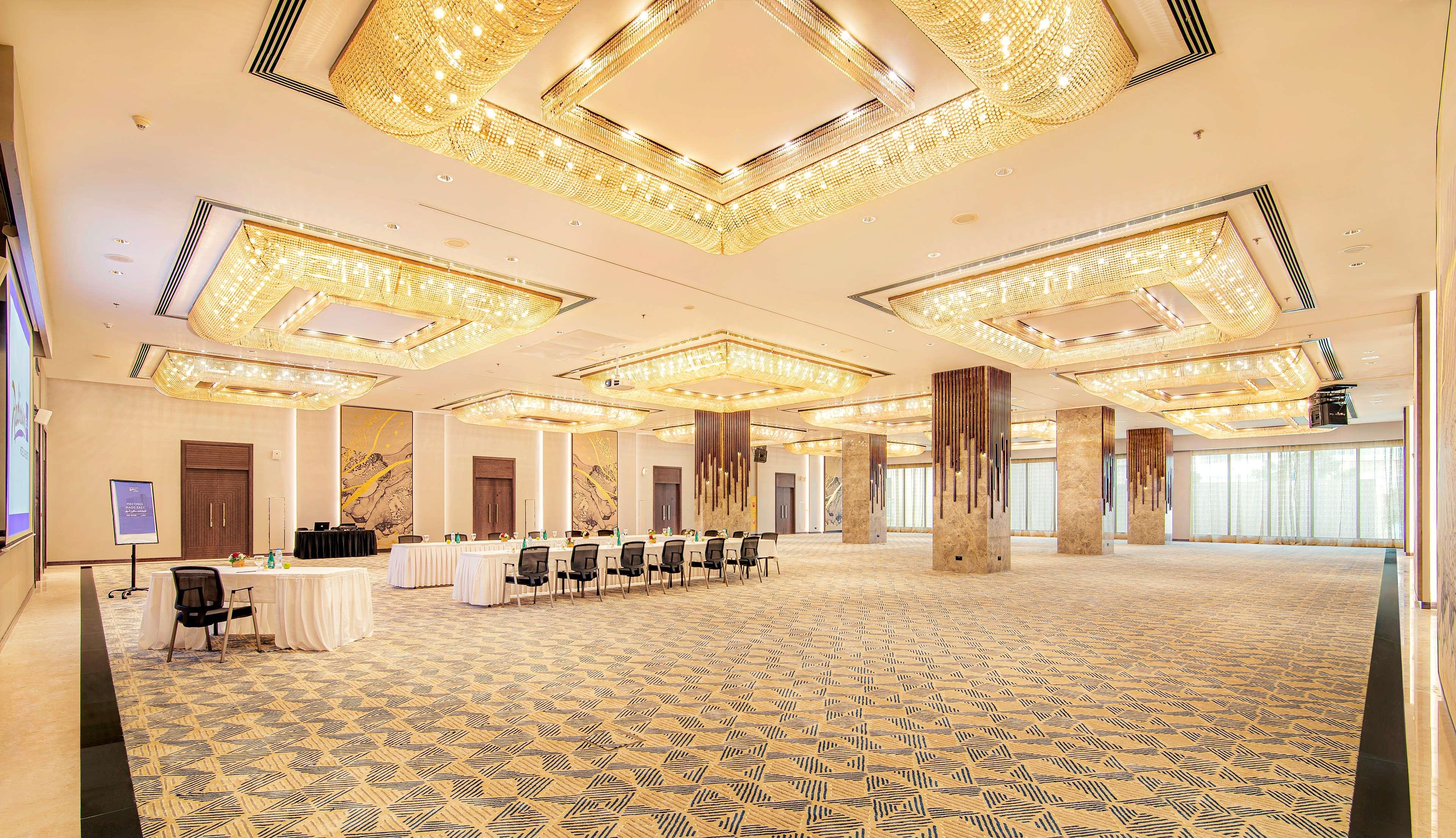 Radisson Blu Hotel & Resort, Abu Dhabi Corniche Extérieur photo The photo shows an elegant event space or banquet hall with a spacious layout. The ceiling features intricate designs and is adorned with multiple chandeliers that provide ample lighting. The floor has an artistic carpet pattern. To one side, there a