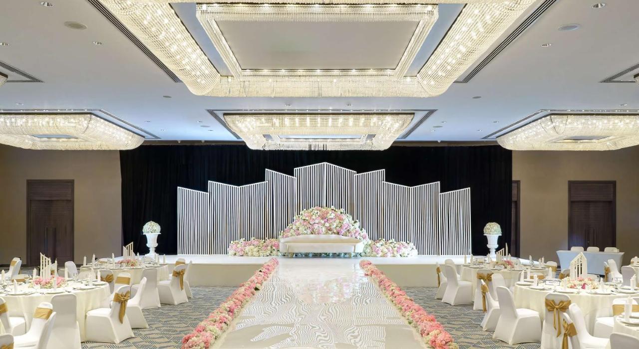 Radisson Blu Hotel & Resort, Abu Dhabi Corniche Extérieur photo The photo depicts a beautifully arranged wedding or event venue. In the center, there is a stage adorned with decorative elements, including a backdrop made of white and silver panels and a floral arrangement featuring pastel-colored flowers. The ais