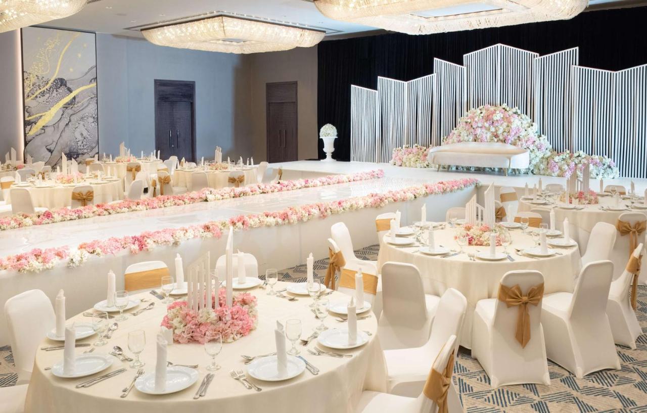 Radisson Blu Hotel & Resort, Abu Dhabi Corniche Extérieur photo The photo shows a beautifully arranged banquet setting. There are round tables with white tablecloths, each adorned with elegant table settings, including plates and candles. The centerpiece of the room features a long table decorated with floral arr