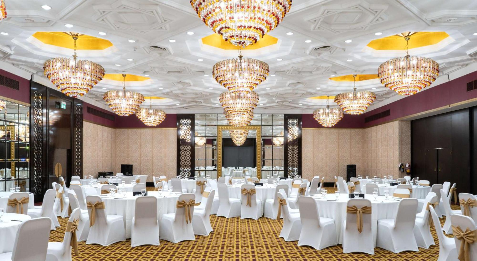 Radisson Blu Hotel & Resort, Abu Dhabi Corniche Extérieur photo The photo depicts an elegant banquet hall or event space. The room is adorned with multiple large, ornate chandeliers that provide bright, ambient lighting. The tables are set with white tablecloths and chairs covered in white fabric, each decorated 