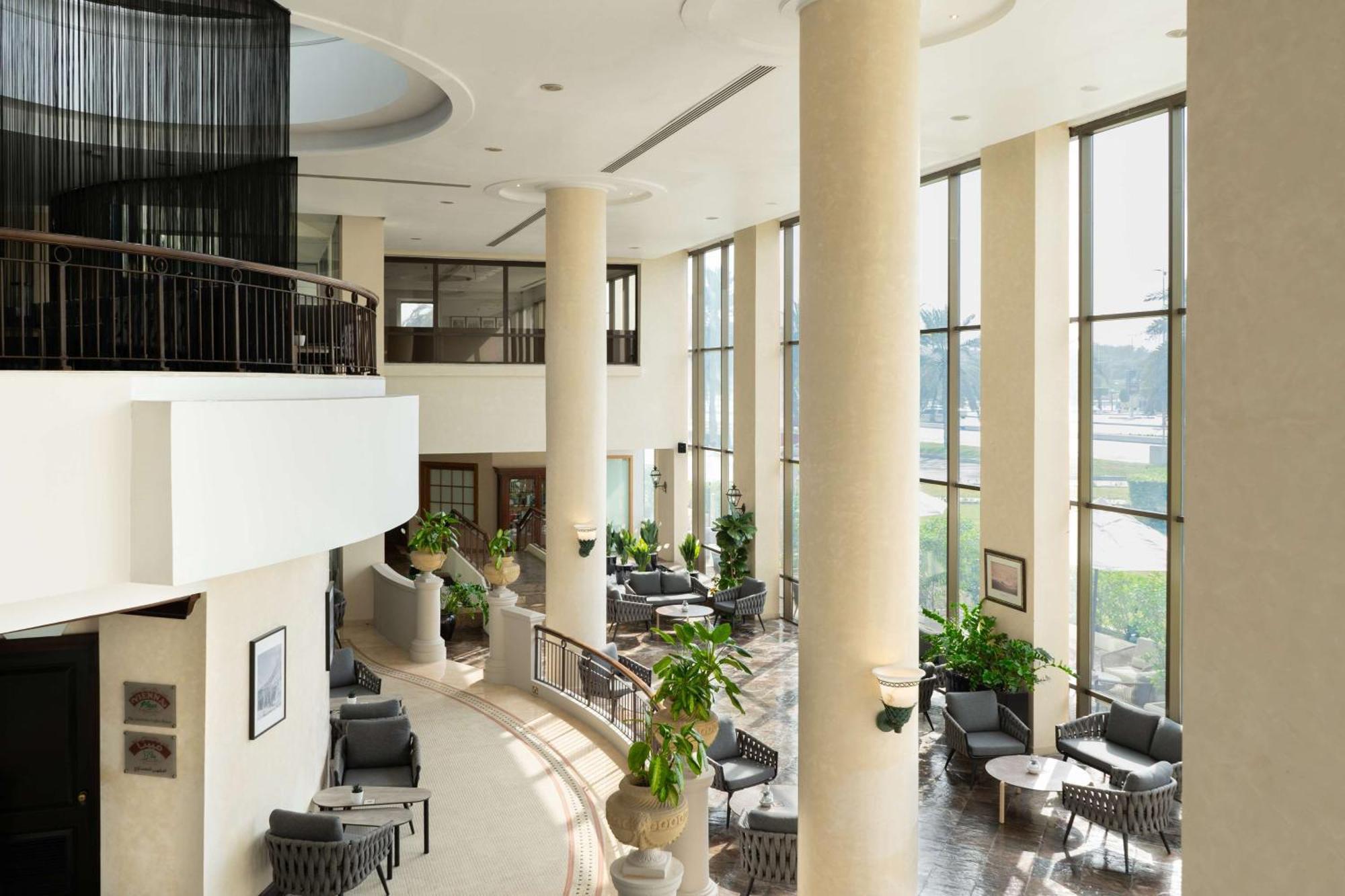 Radisson Blu Hotel & Resort, Abu Dhabi Corniche Extérieur photo The photo shows a spacious, well-lit interior area, likely a lobby or common space in a building. There are tall columns and large windows that let in natural light, creating an airy atmosphere. Comfortable seating arrangements with chairs and small 