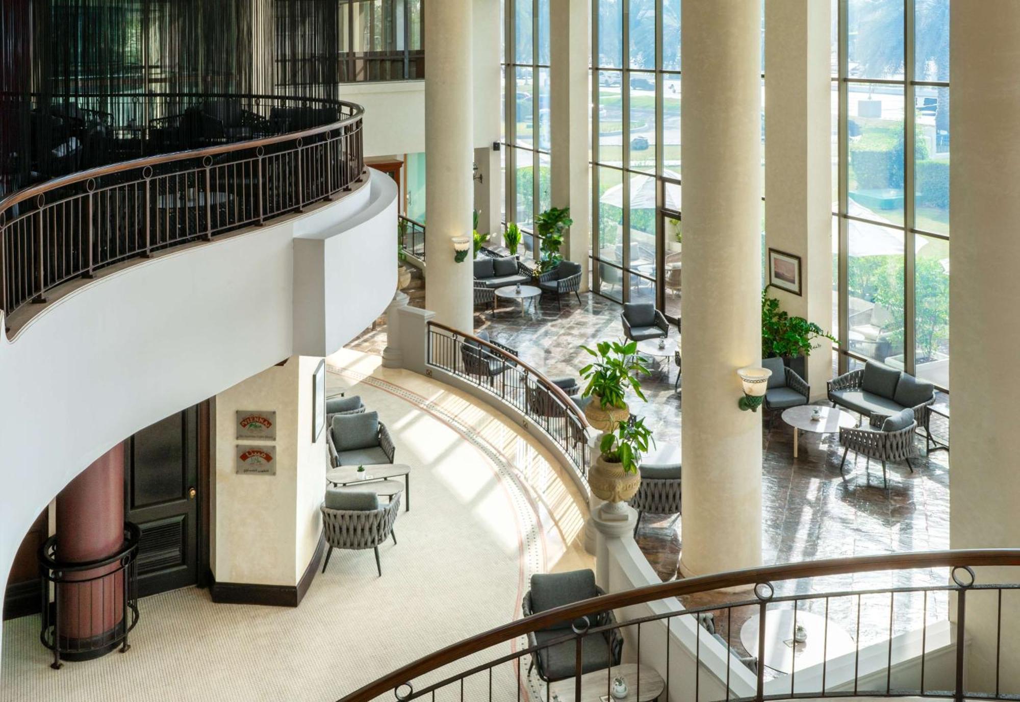 Radisson Blu Hotel & Resort, Abu Dhabi Corniche Extérieur photo The photo depicts a modern interior space, likely within a hotel or a commercial building. It features large windows that allow natural light to flood in, creating a bright and inviting atmosphere. The design includes tall columns and a curved balcon